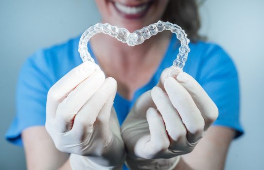 Female doctor holding two transparent heart-shaped dental aligners